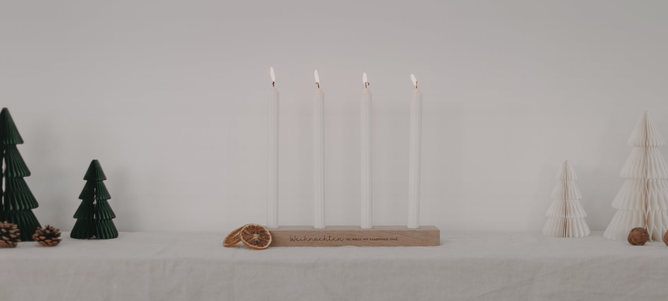 Holzbrett mit vier weißen, brennenden Kerzen. Auf dem Brett steht: ‚Weihnachten ist, wenn wir zusammen sind.‘ Darüber der Text: ‚Für einen zauberhaften Dezember‘. Auf der Schaltfläche darunter steht: ‚Adventsbretter‘