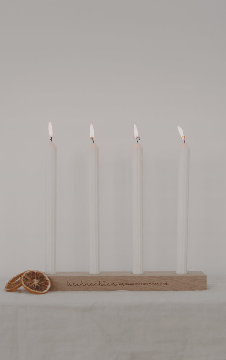Holzbrett mit vier weißen, brennenden Kerzen. Auf dem Brett steht: ‚Weihnachten ist, wenn wir zusammen sind.‘ Darüber der Text: ‚Für einen zauberhaften Dezember‘. Auf der Schaltfläche darunter steht: ‚Adventsbretter‘