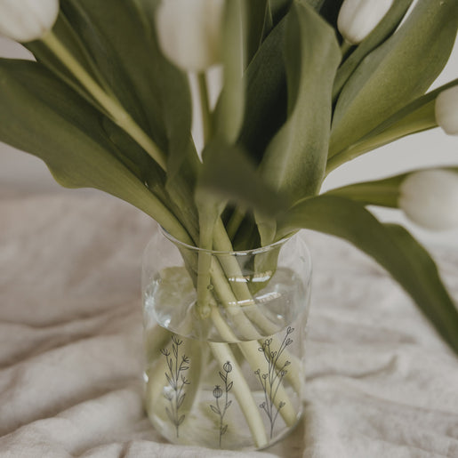 Detailaufnahme einer Glasvase mit filigranem Blumenwiesen-Print und Tulpenstielen im Wasser